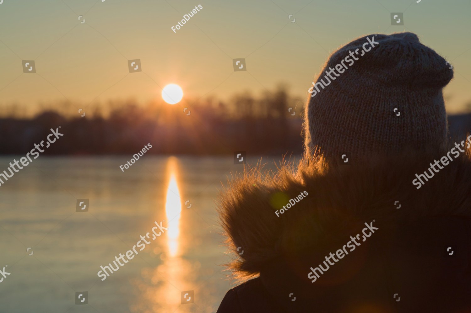 A woman in a knit hat watching the sun set over a lake