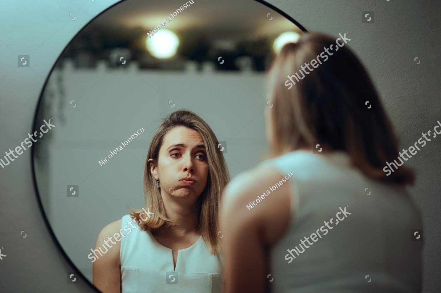A woman looking at her own reflection in a round mirror