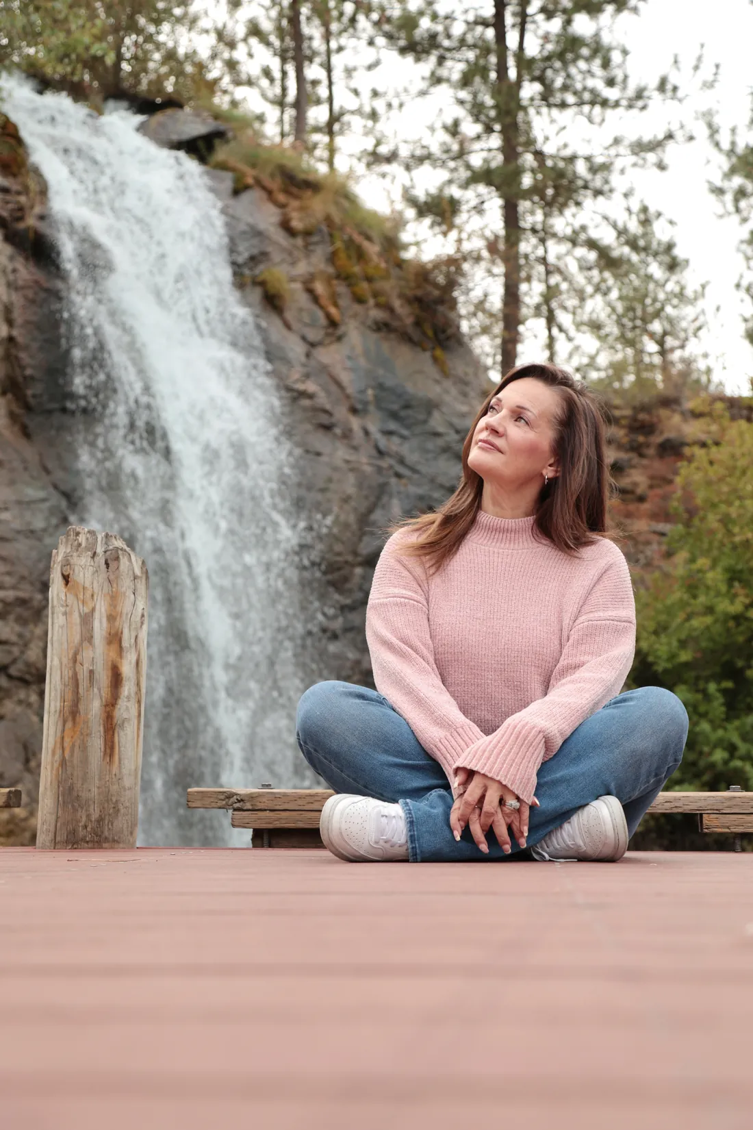 Tye Sheller sitting cross-legged on a wooden deck beside a waterfall