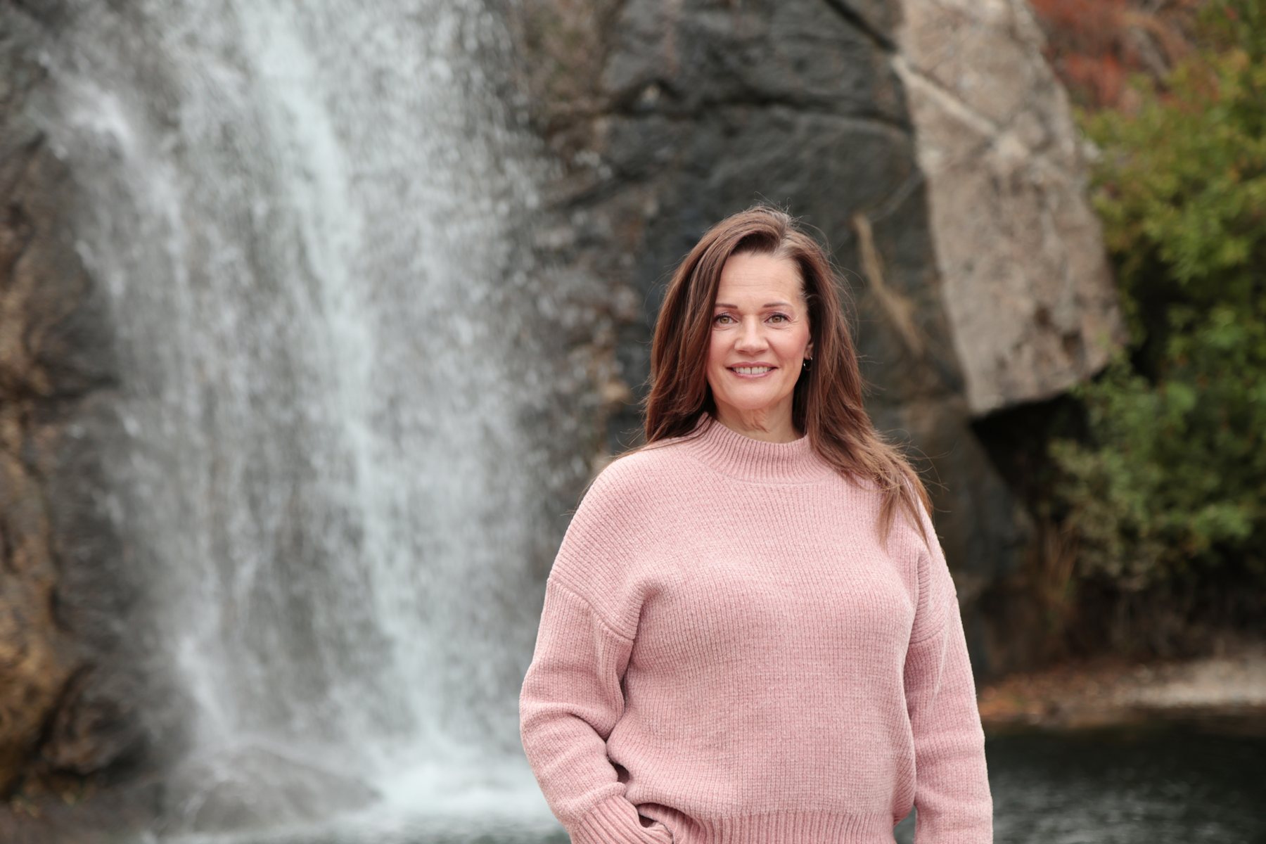 Tye Sheller standing beside a waterfall in a blush sweater